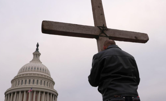 A man stands praying against a cross in front of Congress in Washington