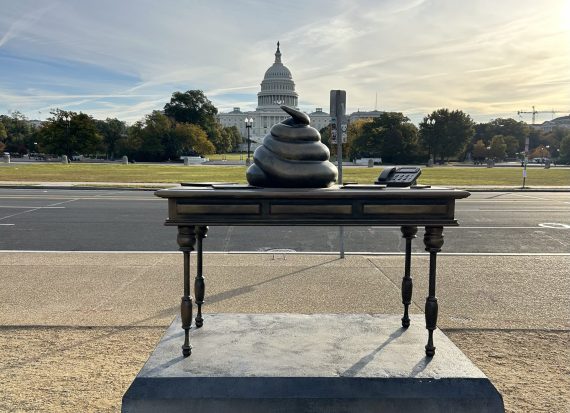 The ironic memorial to the insurrections of Jan 6 featuring a poop emoji on the Resolute Desk, with the Capitol building behind.